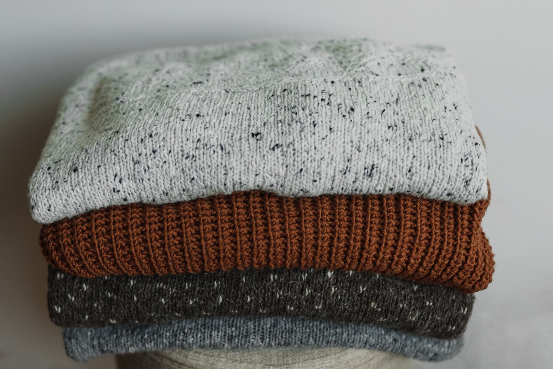 A close view of folded knitwear in neutral tones stacked one piece on another.
