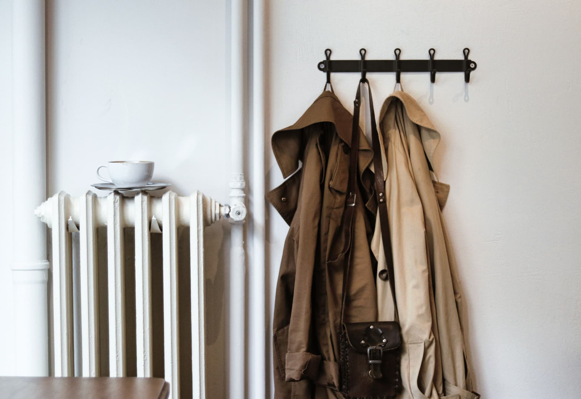 Coats and a bag hanging from a row of hooks beside a radiator in a hallway.